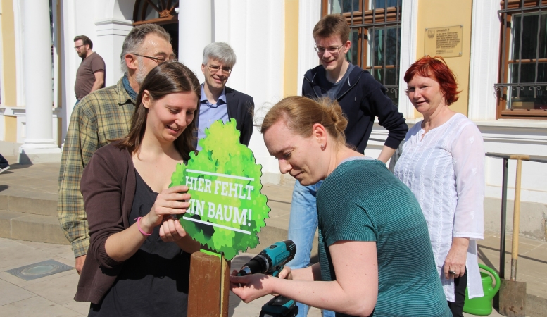 Vor dem Landtag wird an einem Pfahl ein  Baumsymbol angeschraubt.