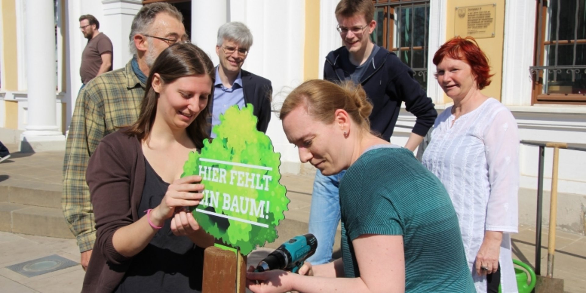 Vor dem Landtag wird an einem Pfahl ein  Baumsymbol angeschraubt.