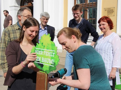 Vor dem Landtag wird an einem Pfahl ein  Baumsymbol angeschraubt.