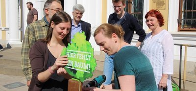 Vor dem Landtag wird an einem Pfahl ein  Baumsymbol angeschraubt.