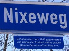 Straßenschild am Nixeweg mit dem Zusatz: Benannt nach dem 1912 gegründeten und damals im Freibad Hellas aktiven Dámen-Schwimm-Club Nixe e. V.